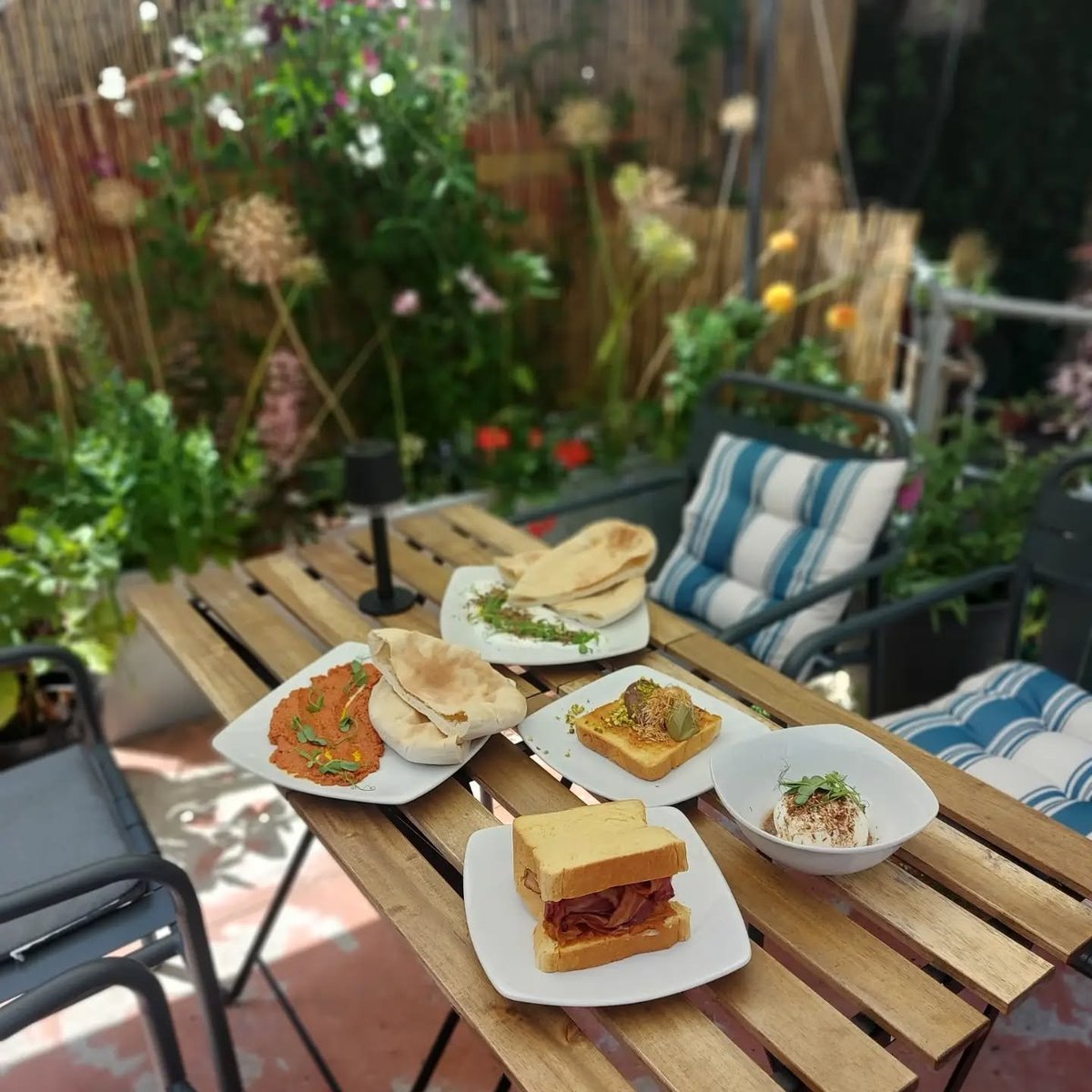 Wadhams outdoor patio with plated wraps, pitta and bread on a wooden table with striped blue chairs and flowers