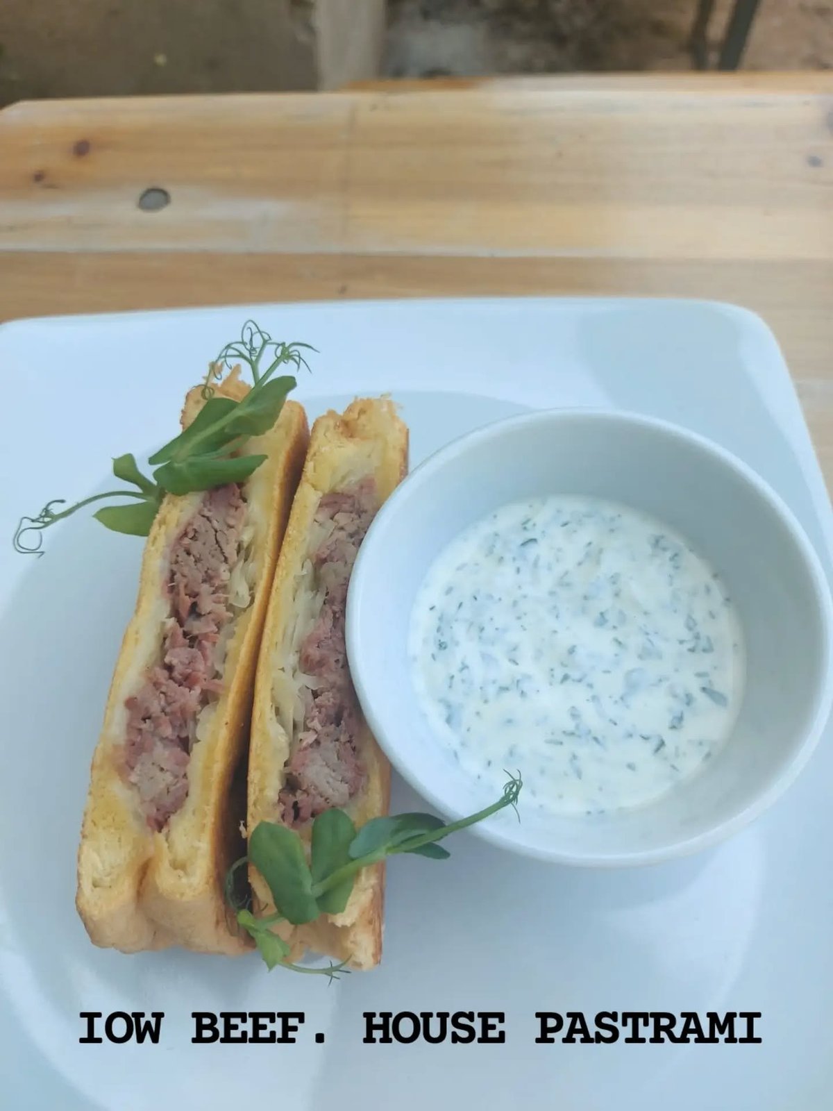 IOW beef house pastrami sandwich on a white plate with herb sauce and microgreens