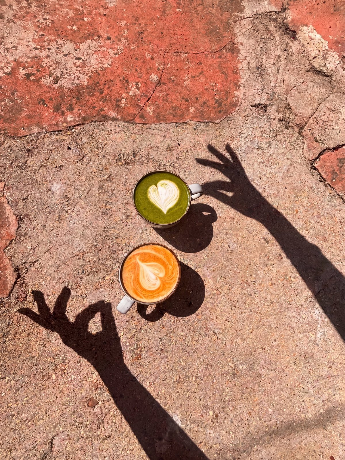 Two coffee cups with latte art on a textured ground, hand shadows in the sunlight